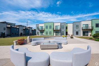 A modern outdoor seating area with a fire pit in front of a row of townhouses.